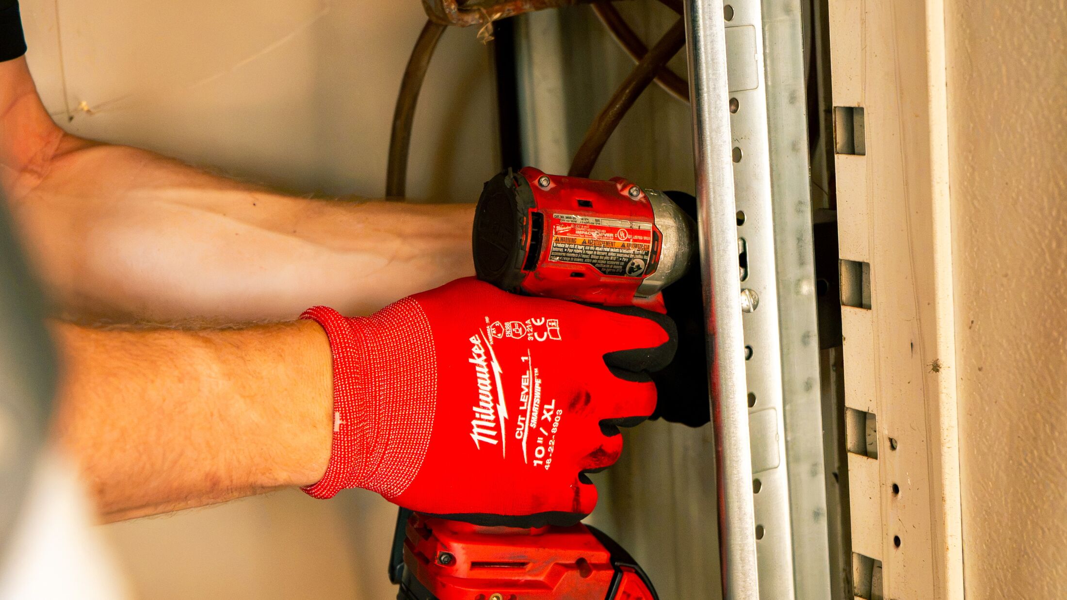 Close-up of a gloved hand and impact driver at a garage door's vertical track